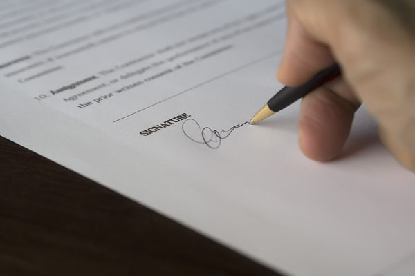 Ręka trzymające długopis, składająca podpis na umowie.