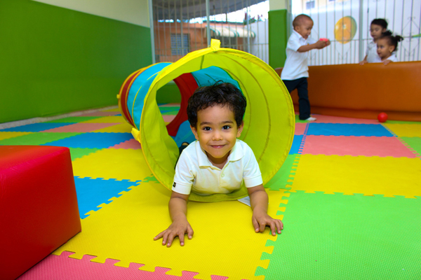 uśmiechnięte dziecko przechodzące przez tunel sensoryczny w pokoju wyłożonym kolorowymi puzzlami